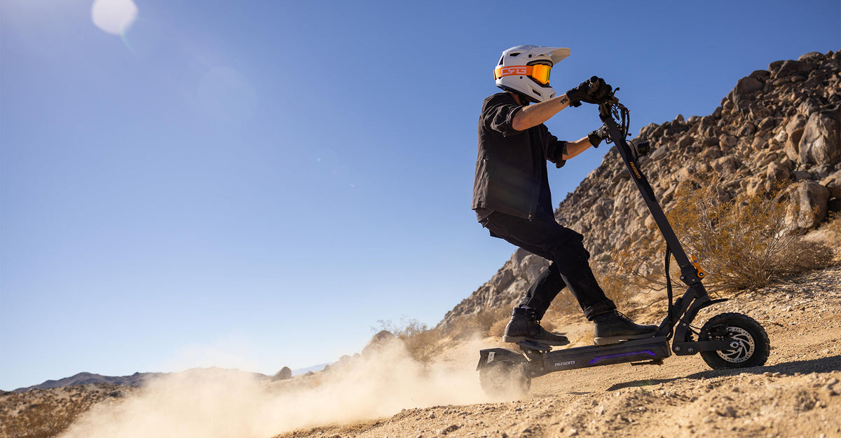 Rider in a white helmet riding an Ausom electric scooter on a dusty desert trail